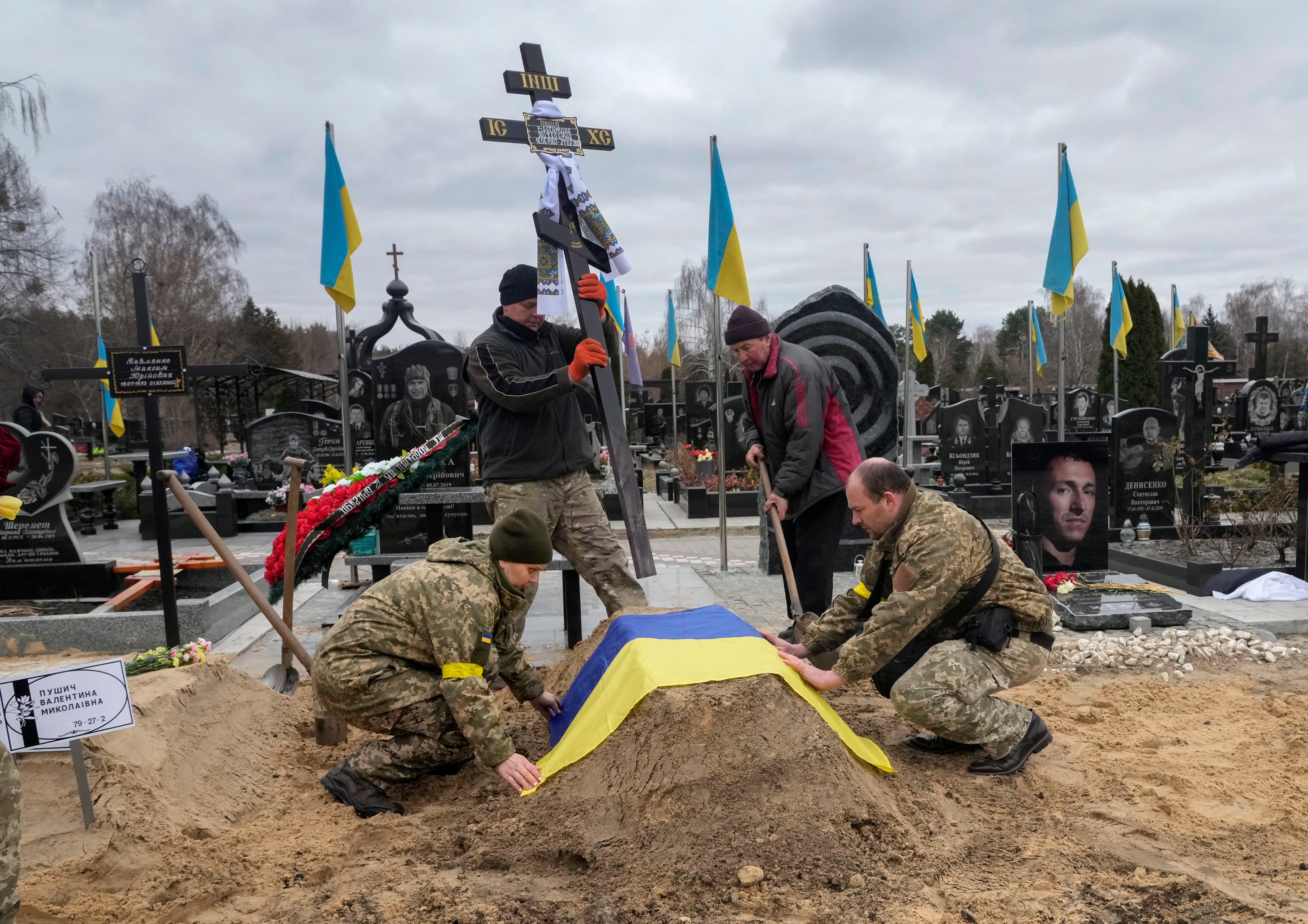 Ukrainian paramedics cover a grave with their country's flag of their colleague Valentyna Pushych, who was killed by Russian troops in a cemetery in Kyiv, Ukraine, Saturday, March 5, 2022. (Efrem Lukatsky/AP)