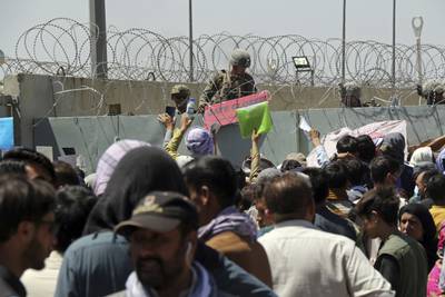 A U.S. soldier holds a sign indicating a gate is closed as hundreds of people gather some holding documents, near an evacuation control checkpoint on the perimeter of the Hamid Karzai International Airport, in Kabul, Afghanistan, Aug. 26, 2021. (Wali Sabawoon/AP)