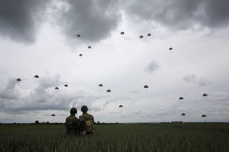 WWII enthusiasts watch French and British parachutists jumping during a commemorative parachute jump over Sannerville, Normandy