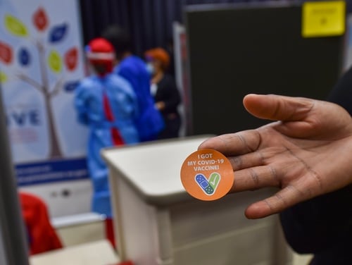 A staffer shows off a COVID-19 vaccination sticker during an event at the Washington, D.C., Veterans Affairs Medical Center on Dec. 15, 2020. (Chief Mass Communication Specialist Charles Hayes/DoD)