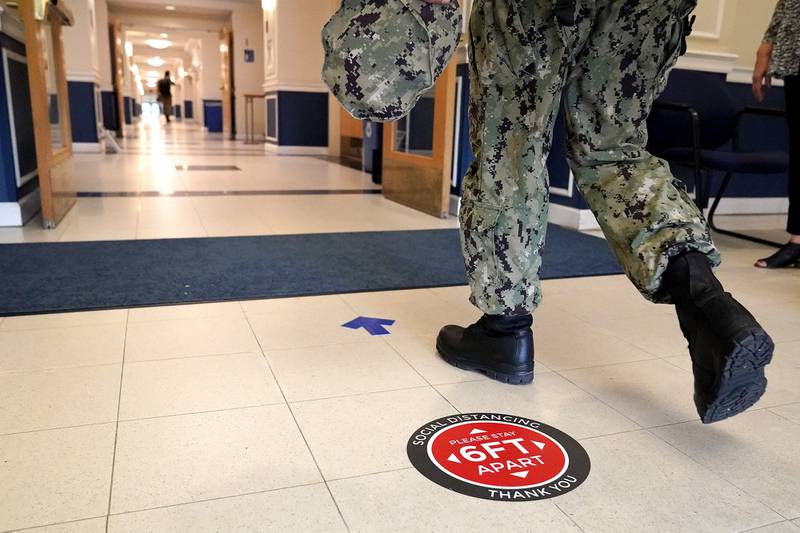 A social distancing sign is seen on the floor as a midshipman walks to class at Luce Hall at the U.S. Naval Academy, Monday, Aug. 24, 2020, in Annapolis, Md.