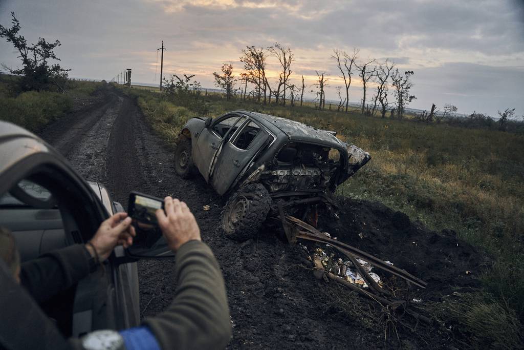 A Ukrainian soldier takes a photo of a burnt car on the road in the freed territory in the Kharkiv region, Ukraine, Monday, Sept. 12, 2022.