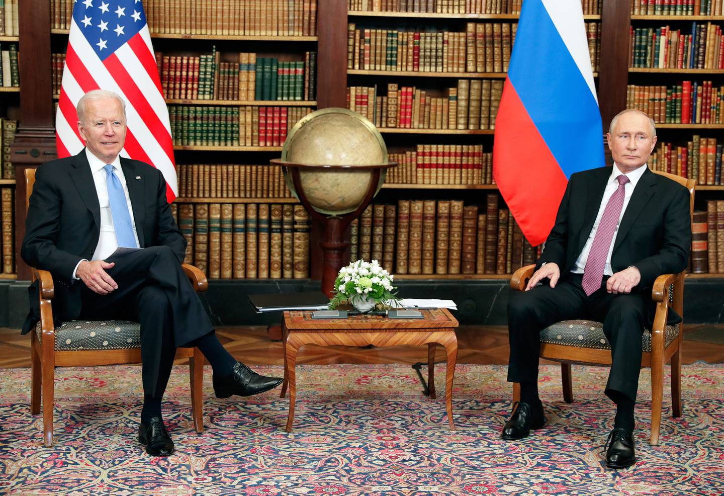 The leaders of the United States and Russia are seated with their nations' flags behind them in a library setting.