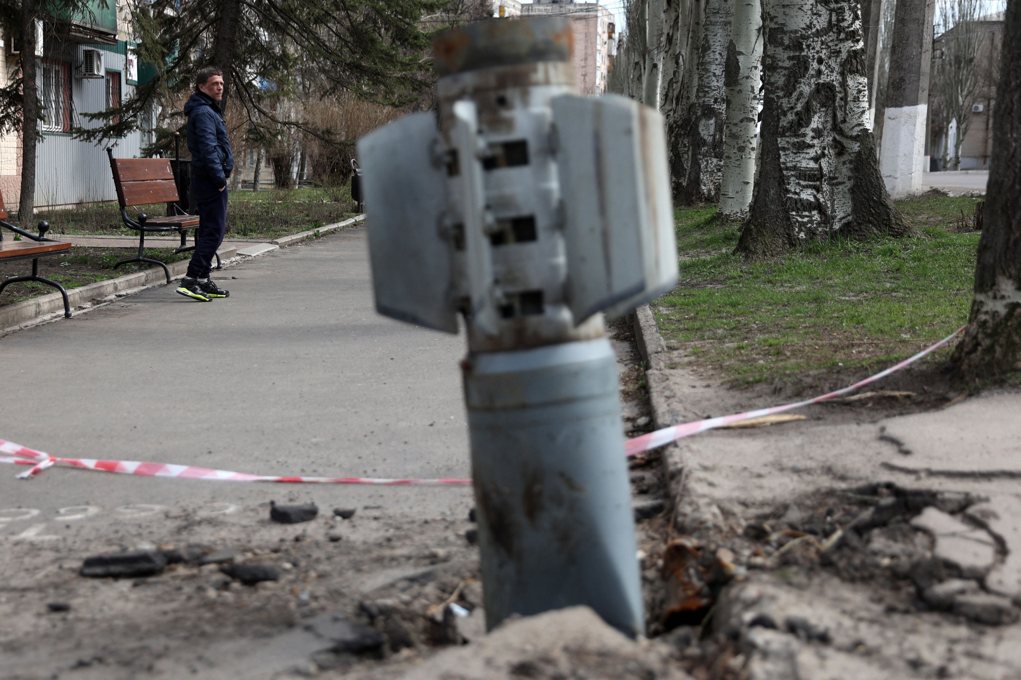 A man walks past an unexploded tail section of a 300mm rocket which appear to contained cluster bombs launched from a BM-30 Smerch multiple rocket launcher embedded in the ground after shelling in Lysychansk, Lugansk region on April 11, 2022. (Photo by ANATOLII STEPANOV/AFP via Getty Images)