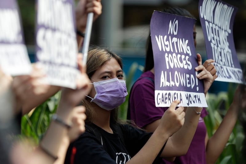 In this March 6, 2020, file photo, a woman protester wearing a protective mask holds a slogan during a rally outside the U.S. Embassy in Manila, Philippines, against the planned military exercises between the Philippines and U.S. under the Visiting Forces Agreement. (Aaron Favila/AP)