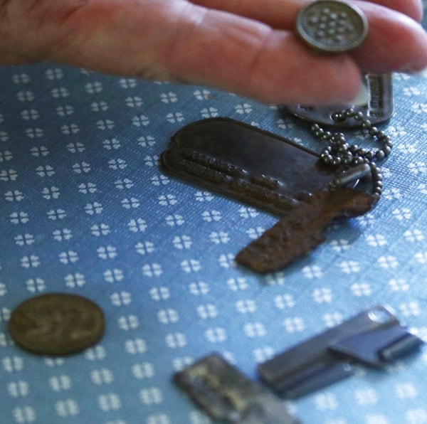 In this July 10, 2018, photo, Mary Beth Seiser handles a button at her home in West Bend, Wis., that was included with her father's dog tags amongst other items. (John R. Ehlke/West Bend Daily News via AP)