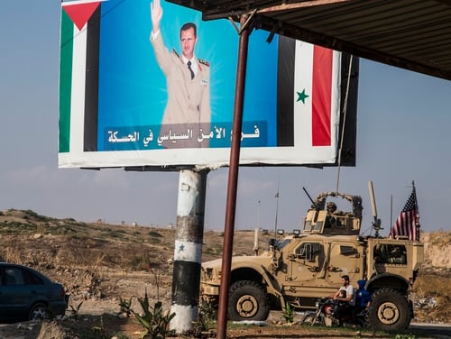 U.S. military convoy drives the he town of Qamishli, north Syria, by a poster showing Syrain President Bashar Aassad Saturday, Oct. 26. 2019. (Baderkhan Ahmad/AP)