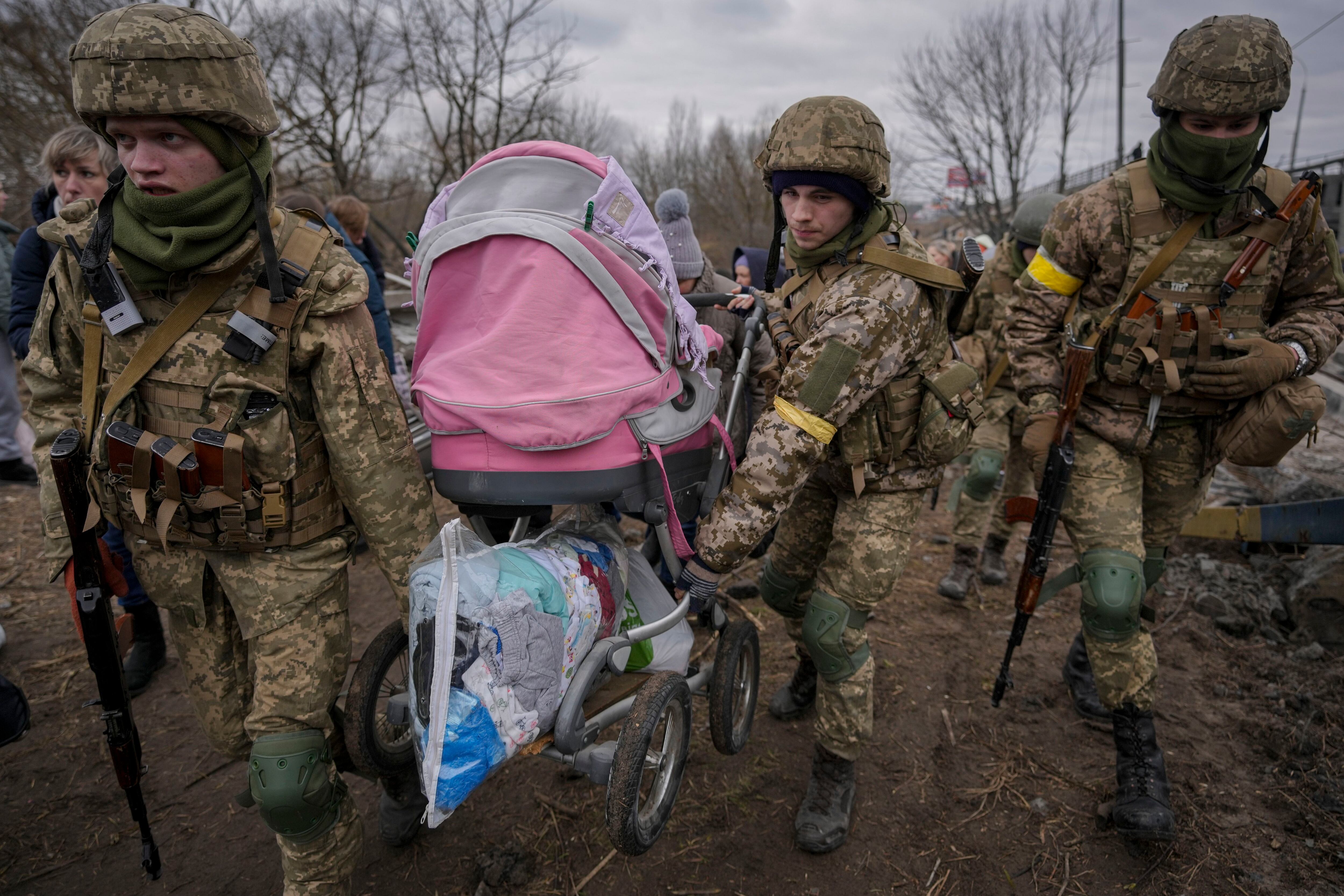 Ukrainian servicemen carry a baby stroller after crossing the Irpin River on an improvised path under a bridge that was destroyed by a Russian airstrike, while assisting people fleeing the town of Irpin, Ukraine, Saturday, March 5, 2022. (Vadim Ghirda/AP)
