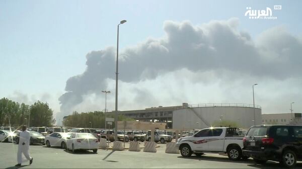 A man walks through a parking lot as the smoke from a fire at the Abqaiq oil processing facility can be seen behind him in Buqyaq, Saudi Arabia, Sept. 14. Drones launched by Yemen's Houthi rebels attacked the world's largest oil processing facility. (Image from video broadcast by Al-Arabiya via AP)
