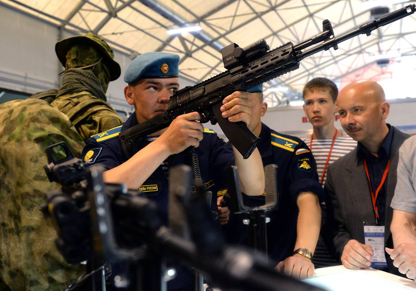 Young cadet holds an AK-12 aloft, examining it's sights at a military exhibition.