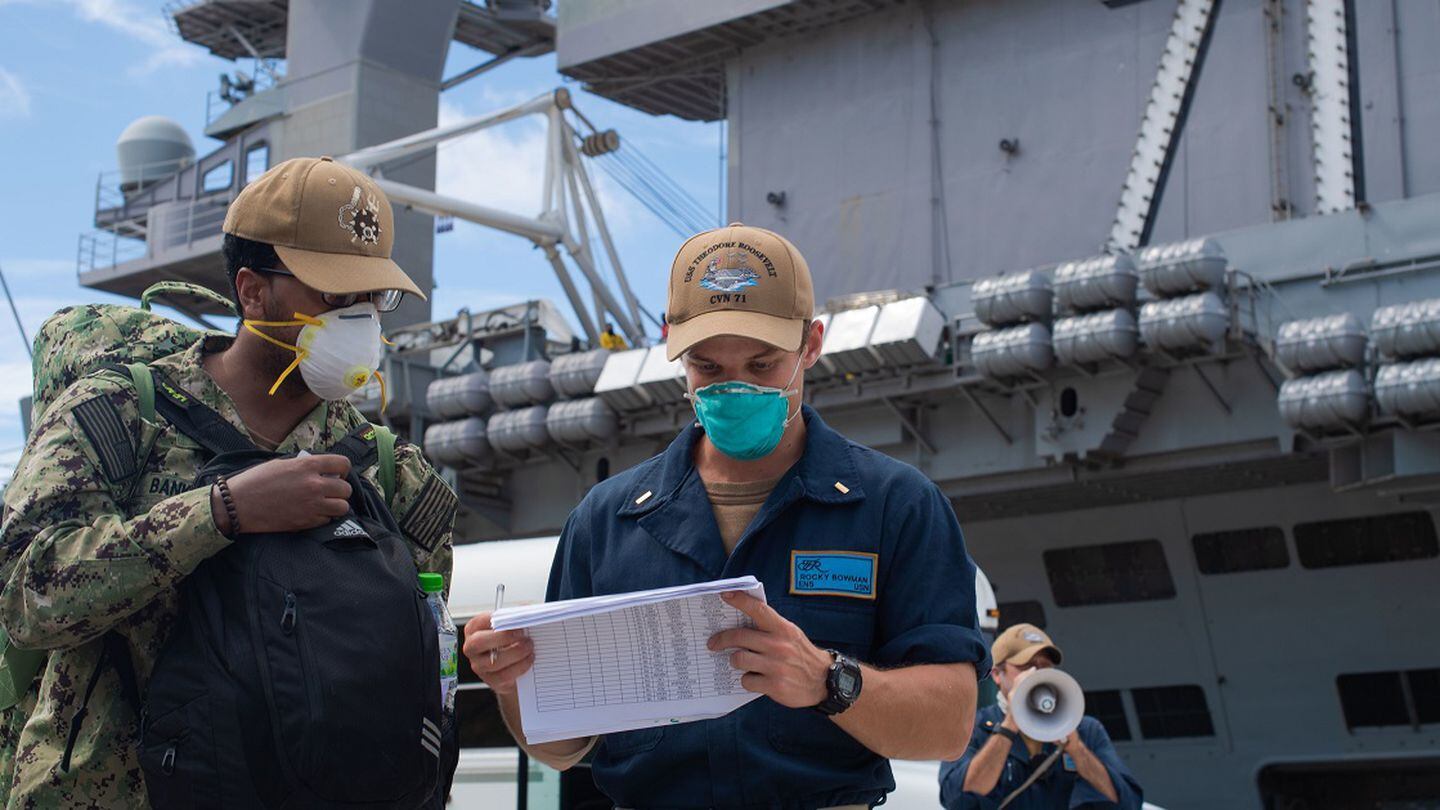 Ensign Rocky Bowman, right, checks Aviation Structural Mechanic 2nd Class Justin Banks onto the aircraft carrier Theodore Roosevelt May 16, 2020, after off-base quarantine. The TR soon continued its deployment to the Indo-Pacific. (MCSN Erik Melgar/Navy)