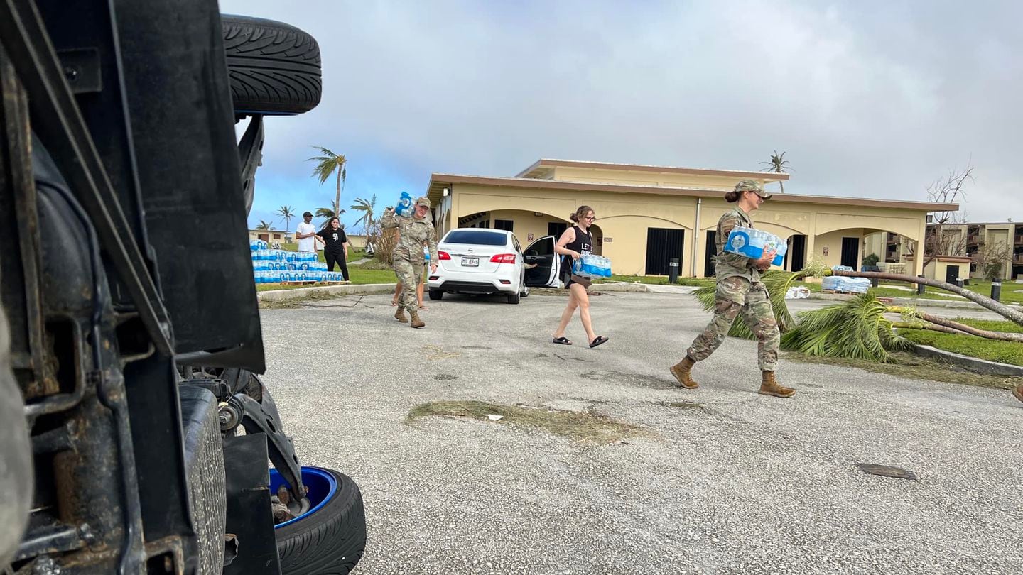 Airmen carry bottled water at Andersen Air Force Base in Guam, passing overturned cars en route. (Air Force)