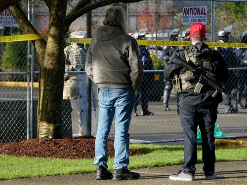 An armed supporter of President Donald Trump looks in at a gathering of Washington State Patrol troopers behind a perimeter fence during a rally, Sunday, Jan. 10, 2021, at the Capitol in Olympia, Wash. (Ted S. Warren/AP)