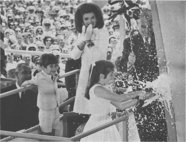 Caroline Kennedy christens the first aircraft carrier named after her father, John F. Kennedy, in 1967. In the background, from left to right: President Lyndon B. Johnson; John F. Kennedy, Jr., Mrs. Jacqueline Kennedy; and Mr. D. A. Holden, President of Newport News Shipbuilding and Drydock Co. (World Wide Photos/U.S. Naval History and Heritage Command)