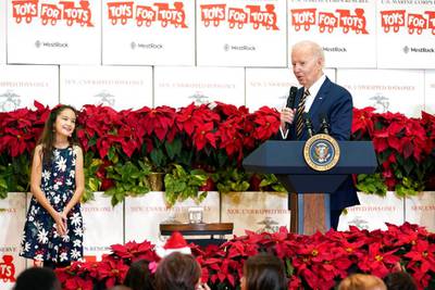 Joe Biden speaking at a Toys for Tots event while a 10-year-old girl listens at the left of the frame