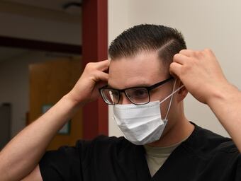 Senior Airman Alexis Lopez, dental assistant with the 319th Medical Group, demonstrates proper sanitary procedure by putting on a face mask at the medical treatment facility at Grand Forks Air Force Base, N.D., in 2017. (Airman 1st Class Elora Martinez/Air Force)