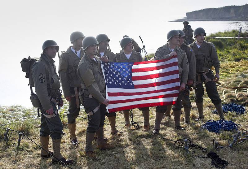 Rangers from the U.S. 75th Ranger Regiment, in period dress, hold the American flag after scaling the cliffs of Pointe-du-Hoc