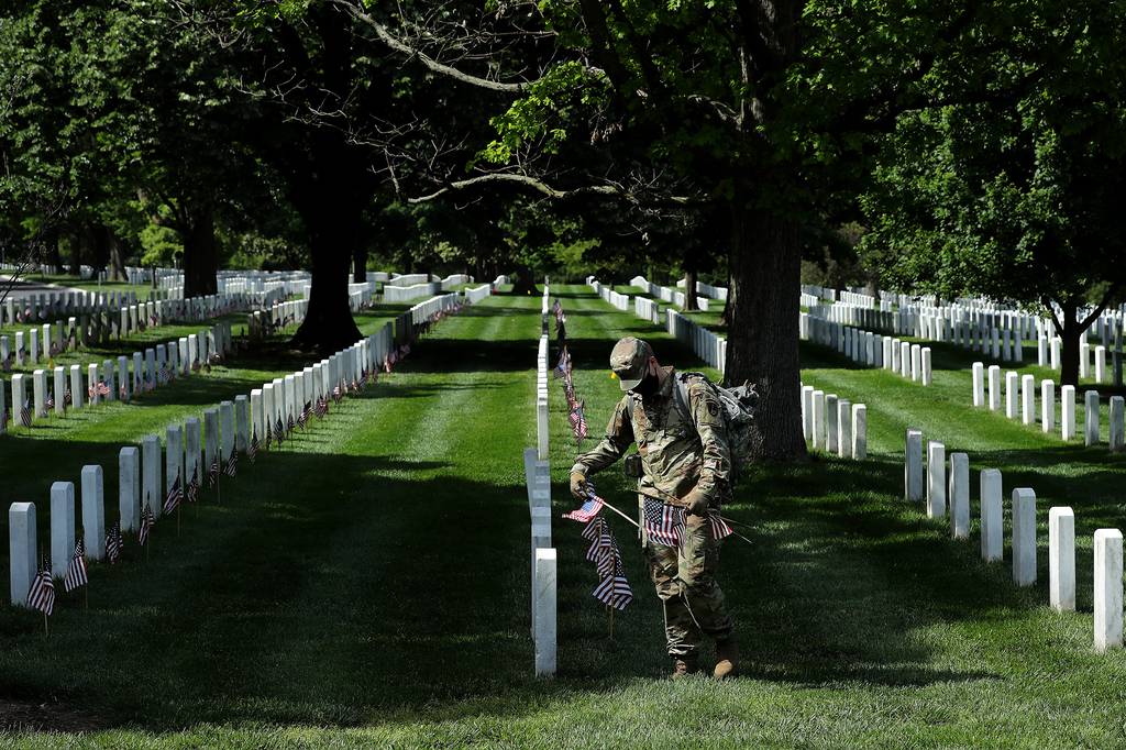 Wearing face masks to reduce the risk of spreading the novel coronavirus, soldiers from the 3rd Infantry Regiment, also called the "Old Guard," place U.S. flags in front of every grave site ahead of the Memorial Day weekend in Arlington National Cemetery on May 21, 2020, in Arlington, Va.