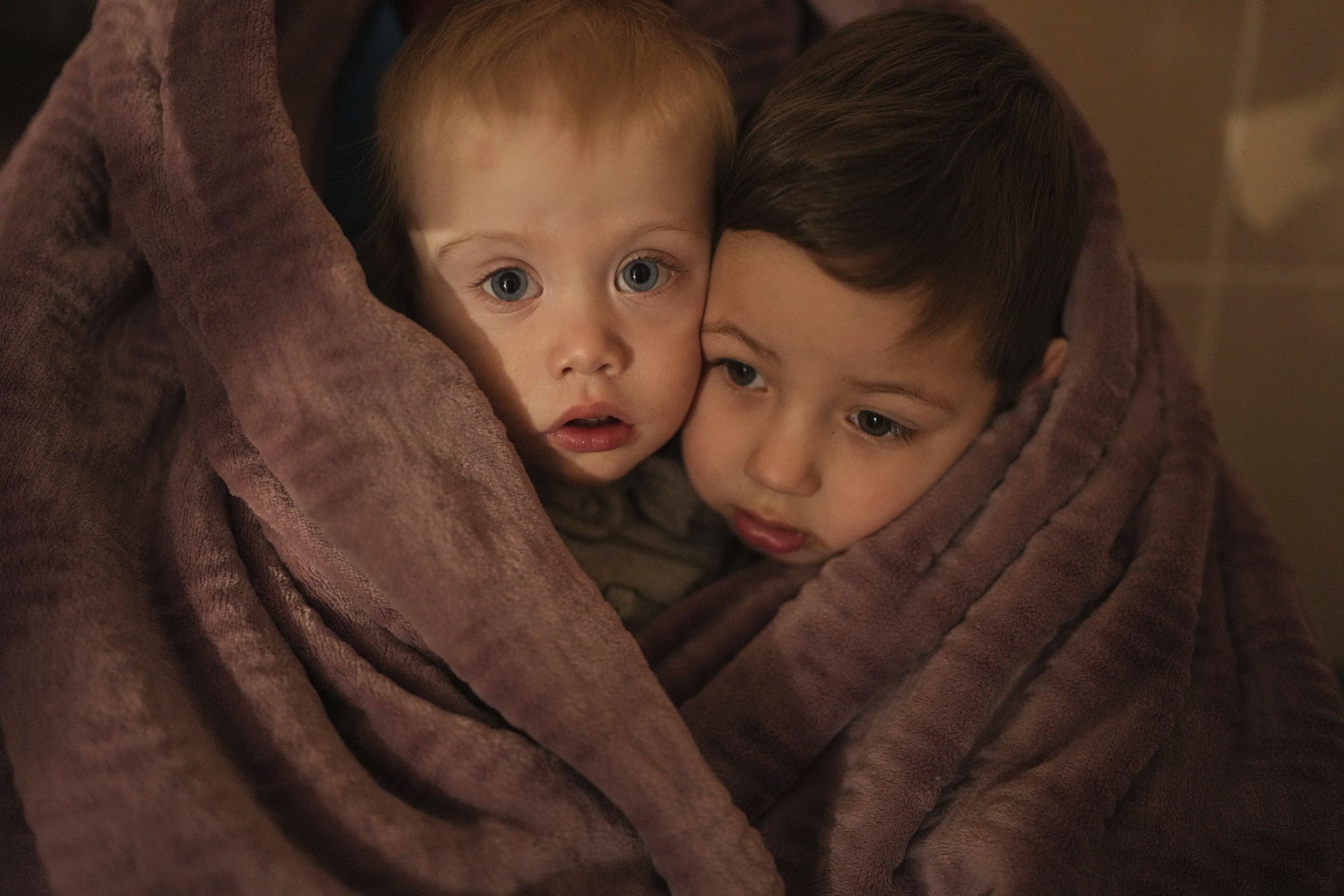 The children of medical workers warm themselves in a blanket as they wait for their relatives in a hospital in Mariupol, Ukraine, Friday, March 4, 2022. (Evgeniy Maloletka/AP)