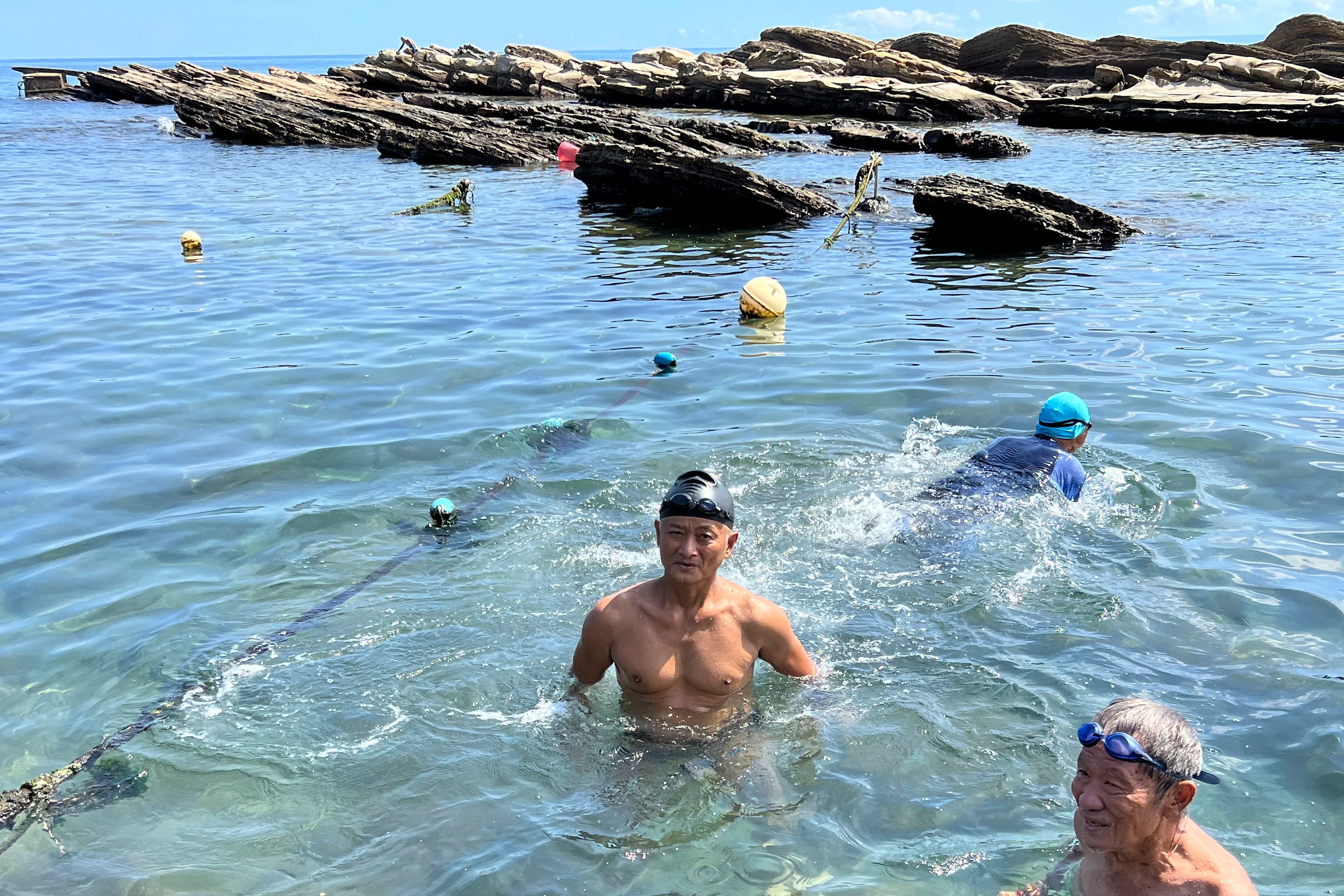 Lu Chuan-hsiong, center, swims along the coast near Keelung in Taiwan, Thursday, Aug. 4, 2022. Lu, 63, who was enjoying his morning swim, says he wasn't worried about the recent China and Taiwan tensions. 