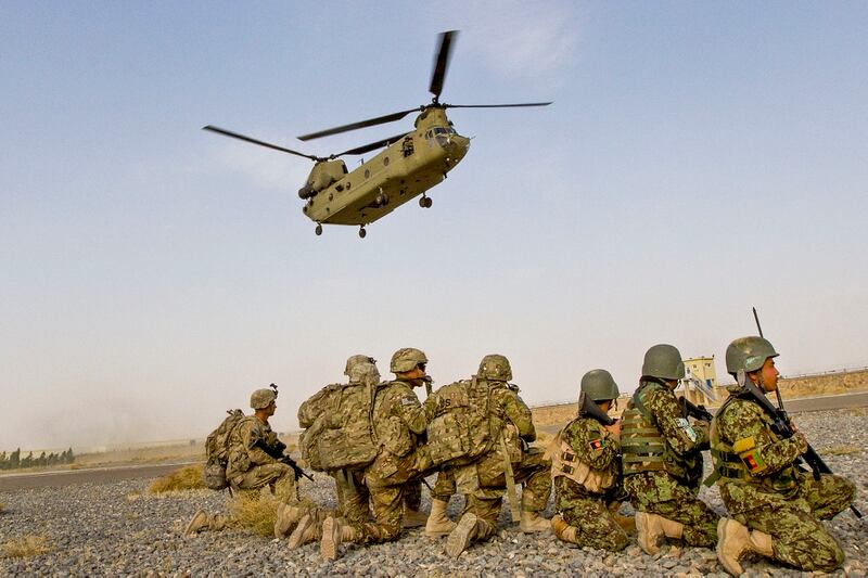 A Chinook helicopter descends over U.S. and Afghan National Army soldiers kneeling in preparation to load the helicopter for a partnered air assault mission to the town of Mirugal Kalay, on Camp Hero, Afghanistan, Oct. 23, 2014. (Sgt. 1st Class Brock Jones/Army)