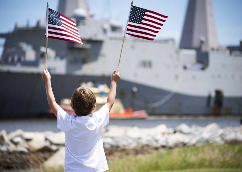A family member waives American flags as the San Antonio-class amphibious transport dock ship USS New York (LPD 21) arrives at Naval Station Mayport in Florida on July 28, 2020.