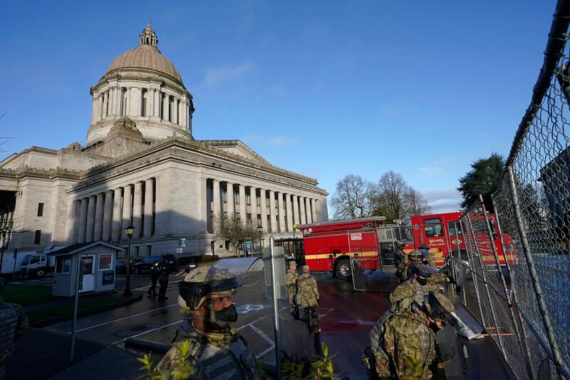 Members of the Washington National Guard stand along a perimeter fence as an Olympia Fire Dept. truck passes by, Sunday, Jan. 10, 2021, at the Capitol in Olympia, Wash. (Ted S. Warren/AP)
