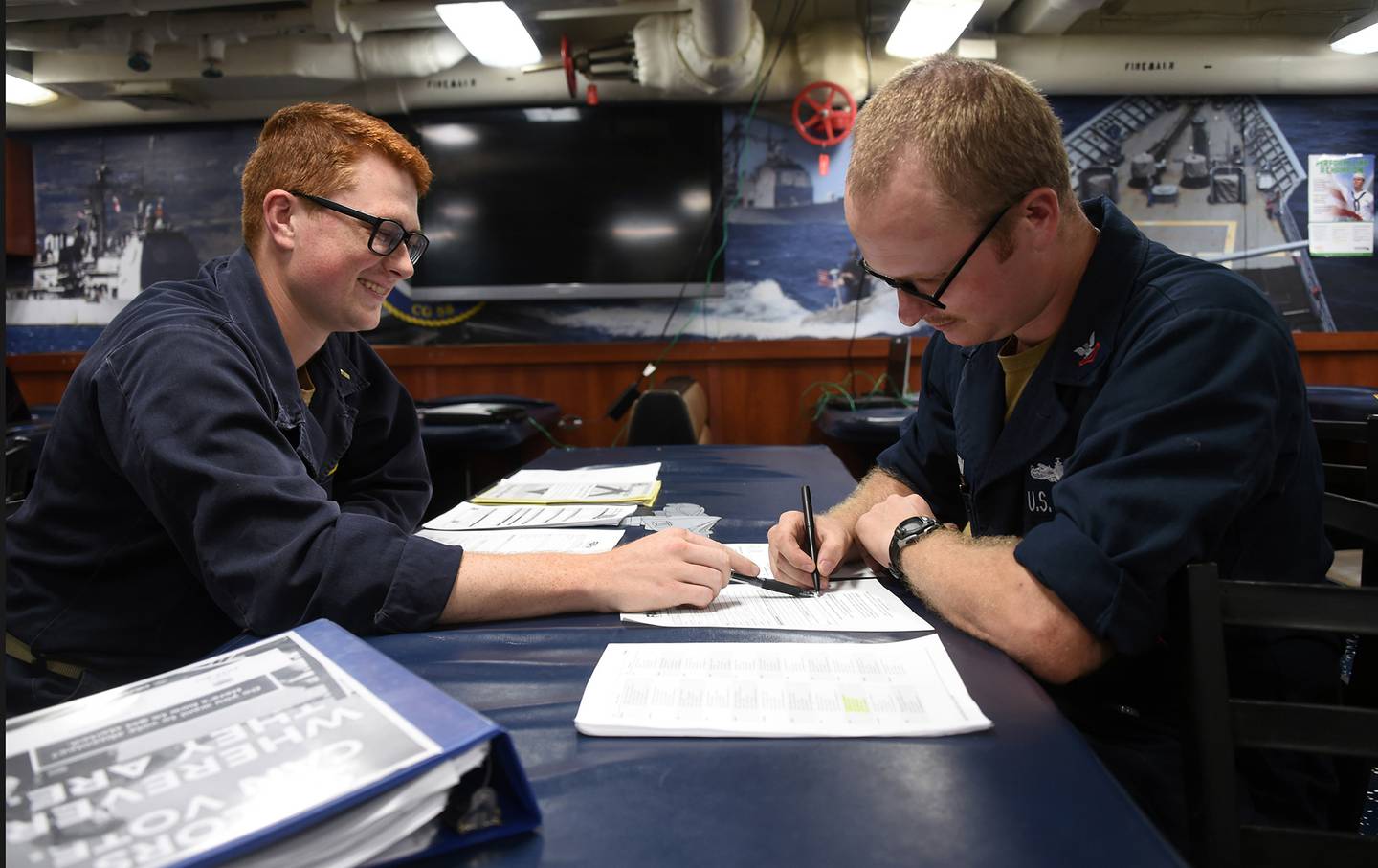 Unit Voting Assistance Officer Ensign Samuel Straub, left, assists Fire Controlman 2nd Class William Vaughn on absentee voting paperwork aboard the mess decks of the Ticonderoga-class guided-missile cruiser USS Philippine Sea (CG 58), Aug. 29, 2020.