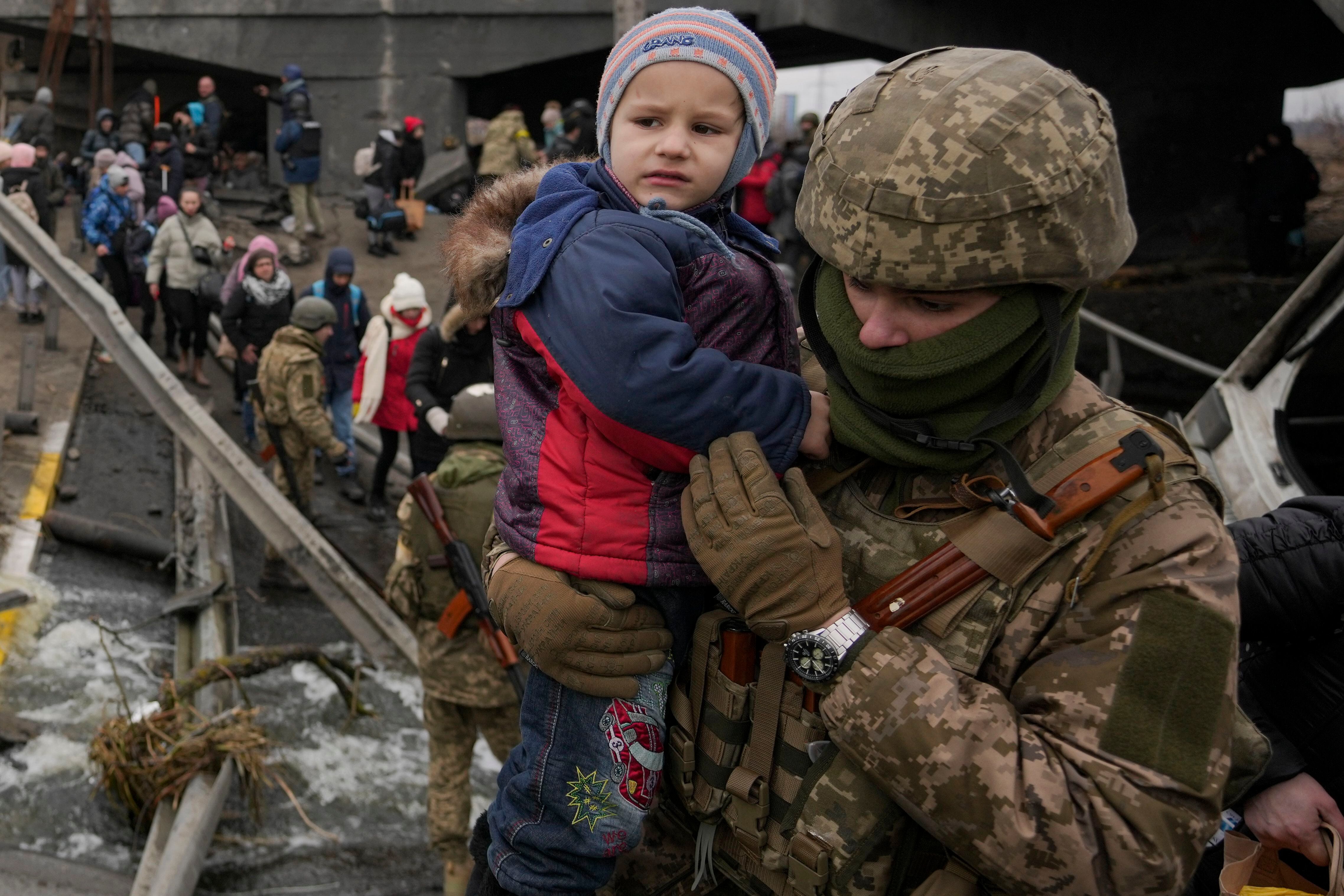 A Ukrainian serviceman holds a baby crossing the Irpin river on an improvised path under a bridge that was destroyed by a Russian airstrike, while assisting people fleeing the town of Irpin, Ukraine, Saturday, March 5, 2022. (Vadim Ghirda/AP)