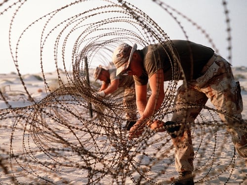 FILE PHOTO: U.S. Marines deploy concertina wire to prevent infiltration of their encampment during Operation Desert Shield. (photo by DOD)