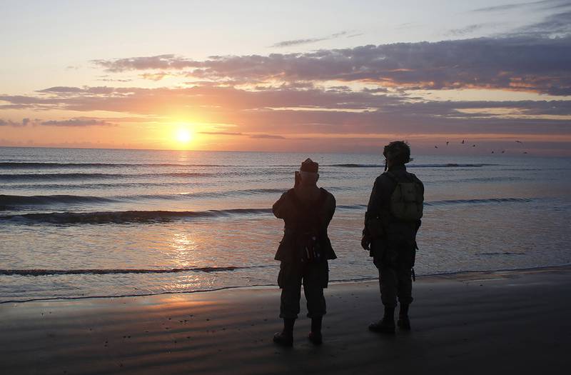 World War II re-enactors stand looking out to sea on Omaha Beach in Normandy, France