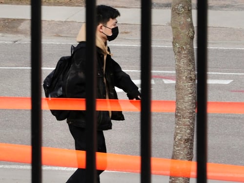 A man wearing a face mask walks past the gates of the University of Vermont Medical Center in Burlington, Vt., on March 12, 2020. (Charles Krupa/AP)