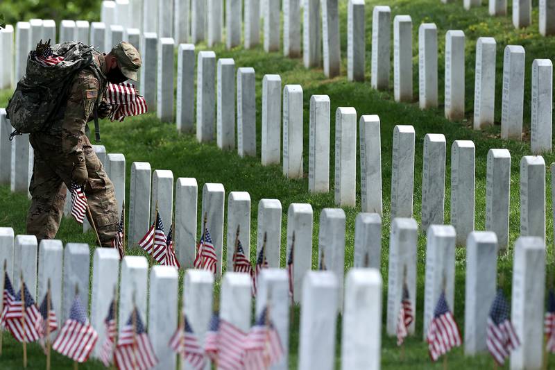 Wearing face masks to reduce the risk of spreading the novel coronavirus, soldiers from the 3rd Infantry Regiment, also called the "Old Guard," place U.S. flags in front of every grave site ahead of the Memorial Day weekend in Arlington National Cemetery on May 21, 2020, in Arlington, Va.