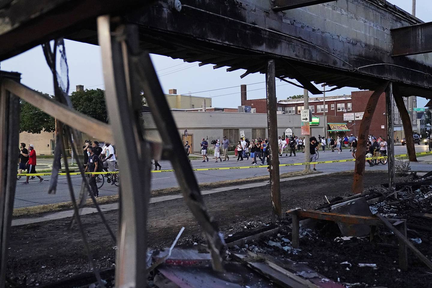 Protesters march past a burned out building damaged in protests against the Sunday police shooting of Jacob Blake in Kenosha, Wis., Wednesday, Aug. 26, 2020.