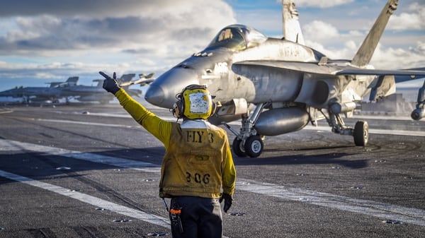 Aviation Boatswain’s Mate (Handling) 3rd Class Vincent Sanchez directs the pilot of an F/A-18C Hornet from the “Blue Blasters” of Strike Fighter Squadron (VFA) 34 on the Nimitz-class aircraft carrier USS Carl Vinson (CVN 70) flight deck in 2017. (Mass Communication Specialist 2nd Class Sean M. Castellano/Navy)