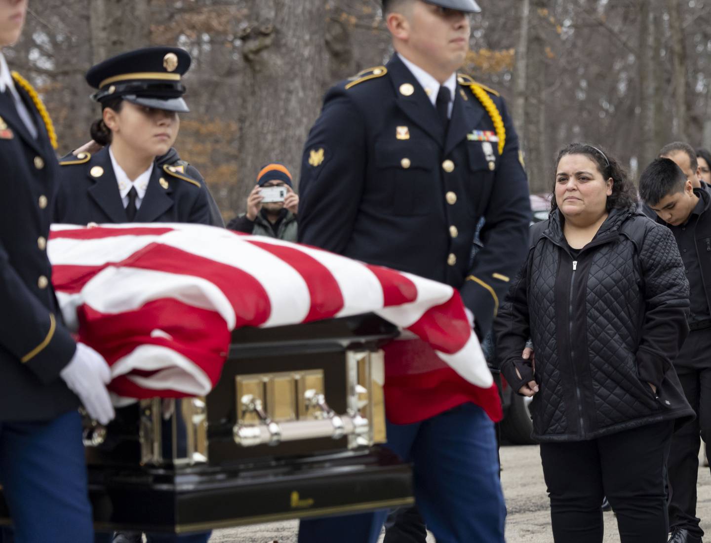 An honor guard carries the casket of former Army Sgt. Joel Gomez while sister Noemi Sanchez watches during funeral services at Abraham Lincoln National Cemetery on Tuesday, Nov. 29, 2022, in Elwood, Ill.