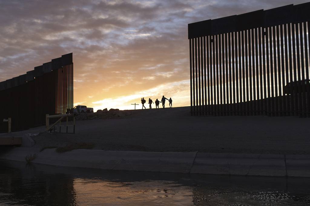 Migrants walk through a gap in the US-Mexico border wall as the sun rises.