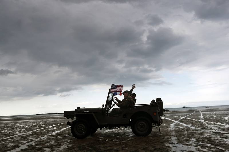 Enthusiasts ride a jeep on the beach of Arromanches