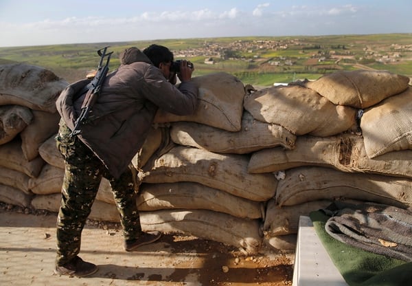 A fighter from the U.S.-backed SDF looks through his binoculars to Turkish-backed fighters' positions at the front line of Halawanji village, north of Manbij, Syria, in March 2018. (Hussein Malla/AP)