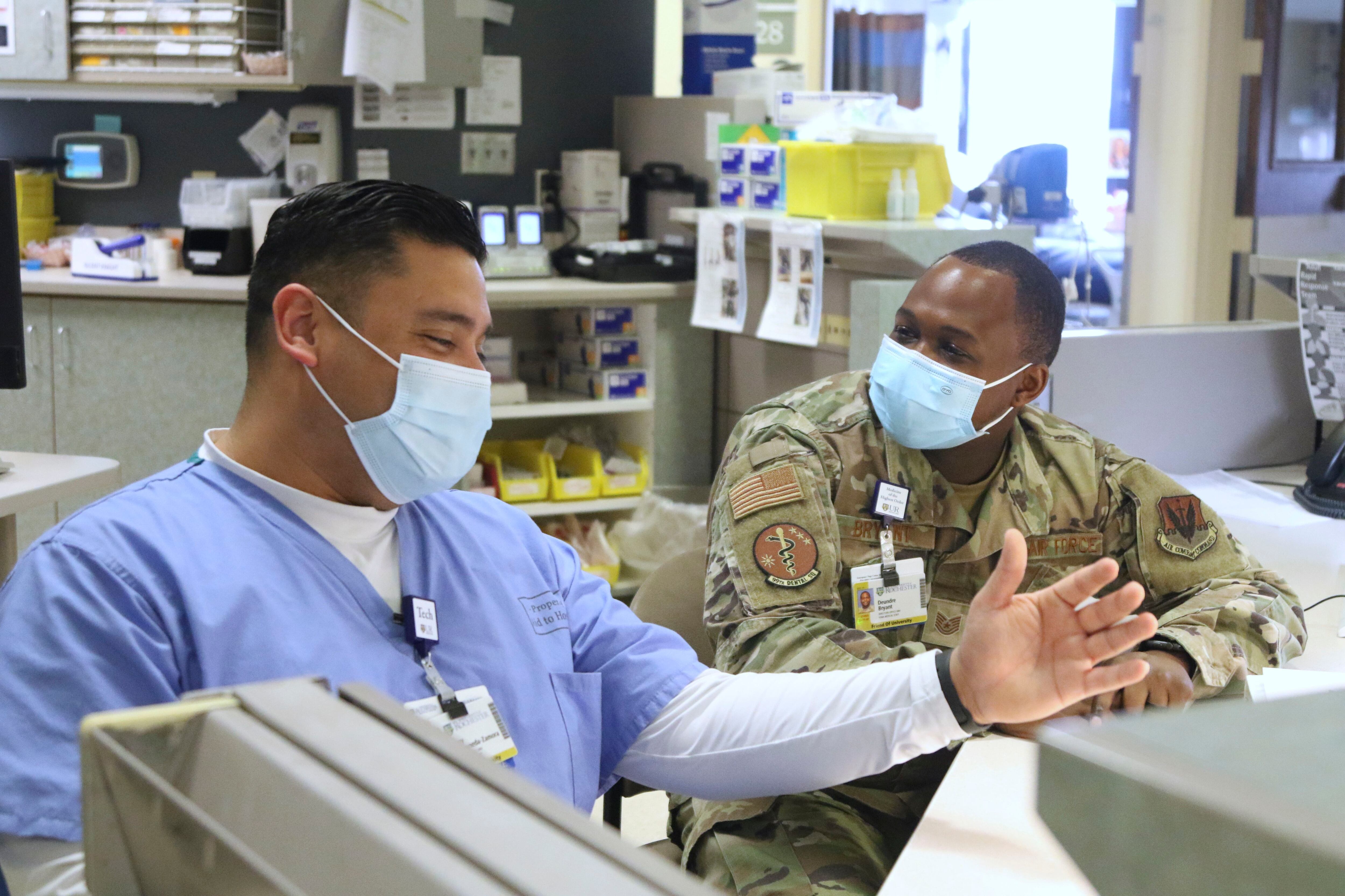 In this image provided by the U.S. Army, U.S. Air Force Tech Sgt. Deundre Bryant, right, a medical administrator, checks up on Tech Sgt. Rony Castaneda-Zamora a medical technician, while supporting the COVID response operations at University of Rochester Medical Center, Rochester, N.Y., Feb.16, 2022. (Spc. Khalan Moore/U.S. Army via AP)