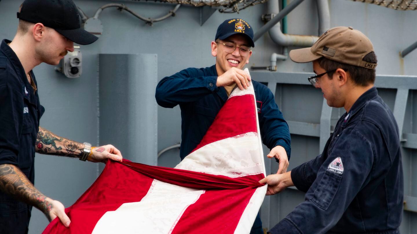 Sailors fold an American flag aboard the amphibious assault ship Tripoli on Sept. 4, 2022. (MC3 Maci Sternod/Navy)