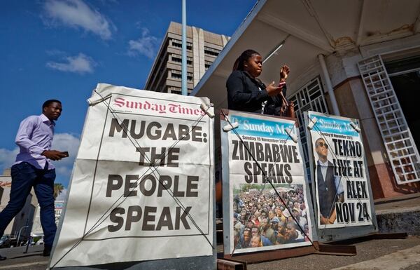 Pedestrians check their mobiles as they walk past a newspaper stand on a street in downtown Harare, Zimbabwe Sunday, Nov. 19, 2017. (Ben Curtis/AP)