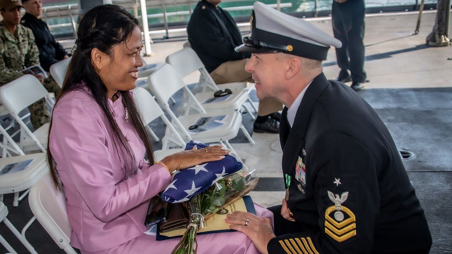 Navy Senior Chief Electricians Mate Matthew P. Dean, senior enlisted leader of Maritime Expeditionary Security Squadron 11, presents an American flag to his wife, Ratda, during his Dec. 2, 2022, retirement ceremony onboard the battleship Iowa. (Chief Boatswain’s Mate Nelson Doromal Jr./Navy)