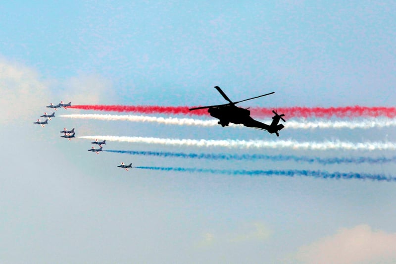 Egyptian Air Force acrobatic jets perform aerial maneuvers with colored smoke as they fly past an Egyptian AH-64 Apache attack helicopter over the capital Cairo on June 2, 2018. (STR/AFP via Getty Images)