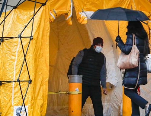 A visitor wearing a face mask waits to be tested for COVID-19 at the main entrance to a New York City Veterans Affairs medical center on March 23, 2020. (John Minchillo/AP)