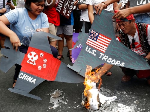 Protesters burn cardboard-cut jet fighters with mock U.S. and China flags as they hold a protest in front of the U.S. embassy in Manila, Philippines on Tuesday. (Aaron Favila/AP)